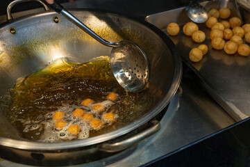 Skimmer ladle lifting golden sweet potato balls while frying in a large steel wok, traditional Taiwanese night market street snack
