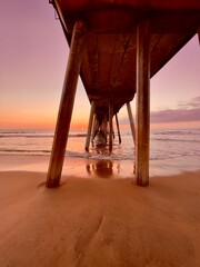 Sunset view under the pier with reflections on wet sand