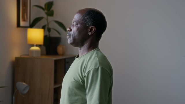 Medium side shot of focused senior African American man standing by work desk in living room, doing weight lifting fitness exercise with heavy stack of books while keeping fit in old age - Powered by Adobe