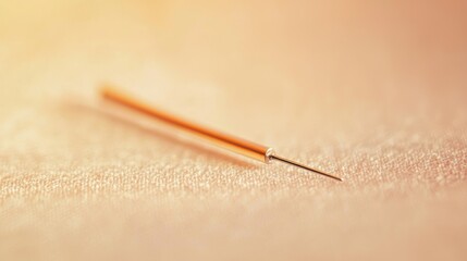 A single gold needle with a sharp point lies on a soft, beige fabric surface, with a blurred background that suggests a soft focus effect.