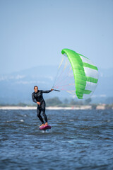 A middle-aged man in a wetsuit glides on a hydrofoil board with a green and white kite
