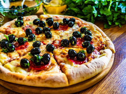 Pizza pepperoni with mozzarella cheese and black olives on wooden table - Powered by Adobe