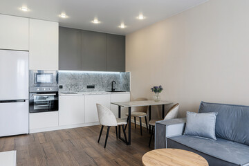 Modern apartment interior: kitchen with white and gray cabinets, dining table with chairs, and a gray sofa