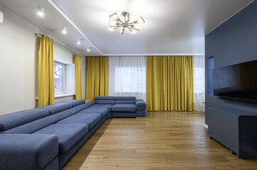 modern living room featuring a large blue sofa, yellow curtains, and wood flooring