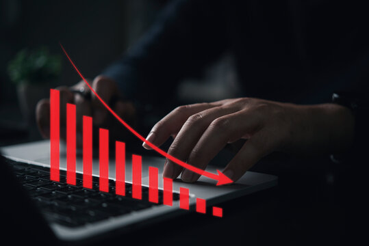 Hands working on computer with falling bar chart in red, representing market decline, financial loss, global crisis, and economic downturn.