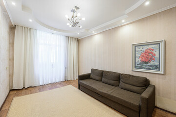 cozy living room with a brown sofa, light carpet, white curtains, and a painting of a ship