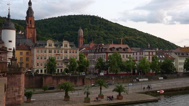 Heidelberg, Germany - June 21, 2025: Iconic Old Bridge and the Karl Theodor Gate in Heidelberg, showcasing houses and vibrant green hills.