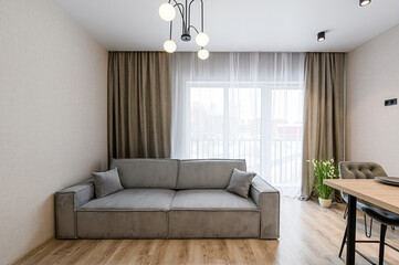 Cozy living room with a gray sofa, curtains, and modern lighting. Minimalist design with a warm color palette and natural light