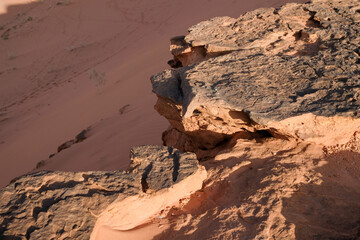 A wide-angle landscape shot of a vast, rocky desert with a large, layered sandstone formation in the foreground and a series of rugged mountains and rolling sand plains stretching into the hazy distan