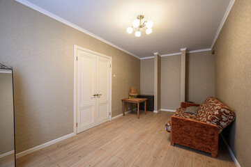 cozy room features neutral wallpaper, wood floors, and white trim. A white double door sits on the left, and a patterned sofa is against the right wall
