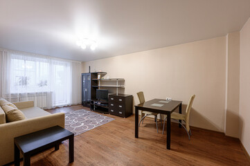 Cozy living room with neutral decor. A sofa sits near a window, with a dining table and...