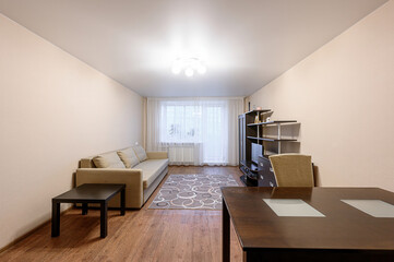 A cozy living room featuring a sofa, a dark wood table, and shelving unit. A circular patterned rug adds a touch of color