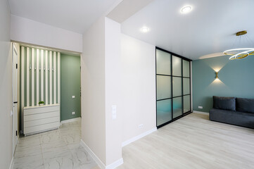 Modern interior with a minimalist design. Features a hallway with striped decor, a sliding glass door, and a seating area with a grey couch and a stylish lighting fixture