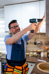 Man installs shelves with power drill in modern kitchen during daytime