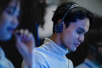 A happy young professional with a headset smiles while working on his computer at night. A concept...