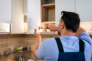 Man repairs kitchen cabinet in modern home during daylight hours for home improvement project
