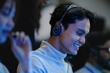 A happy young professional with a headset smiles while working on his computer at night. A concept...