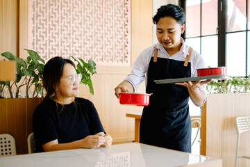 Southeast Asian waiter serving food in red bowls to a woman in a Chinese restaurant