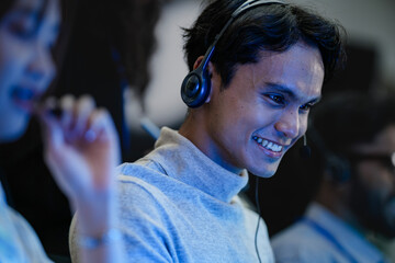 A happy young professional with a headset smiles while working on his computer at night. A concept...