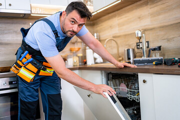 Plumber repairing a dishwasher in a modern kitchen during daytime