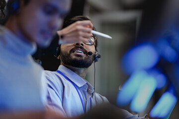 A happy young professional with a headset smiles while working on his computer at night. A concept...
