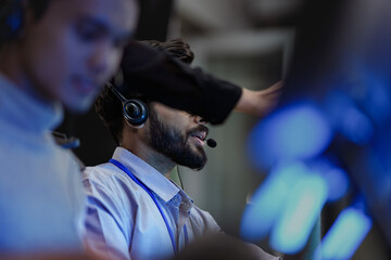 A happy young professional with a headset smiles while working on his computer at night. A concept...