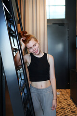 Young woman in casual loungewear smiling and leaning on a ladder indoors