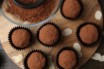 Delicious homemade candies powdered with cocoa on wooden table, flat lay
