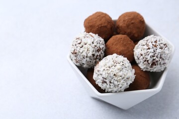 Delicious homemade candies with cocoa powder and coconut flakes in bowl on white table, closeup....