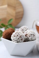 Delicious homemade candies with cocoa powder and coconut flakes in bowl on white table, closeup