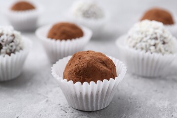 Delicious homemade candies with cocoa powder and coconut flakes on light grey table, closeup