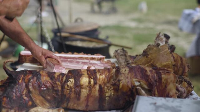 Hands of the chef while using the mincer to cut bacon, roasted whole pig on the table