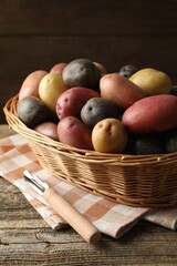 Different types of potatoes in wicker basket on wooden table, closeup
