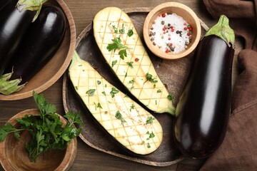 Halves of fresh eggplant, whole ones, spices and parsley on wooden table, flat lay