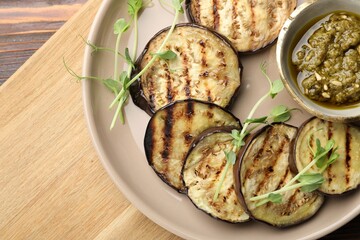 Grilled slices of eggplant with sauce and microgreens on wooden table, top view