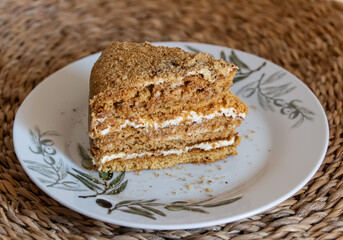 Piece of cake (medovnik) is on a plate. Layered cake, with crumbs around it. Served on a white plate on a wooden place mat. Closeup photograph from above. Version 1.