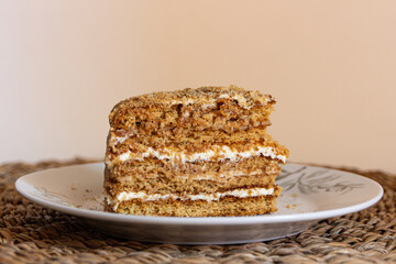 Piece of cake (medovnik) is on a plate. Layered cake, with crumbs around it. Served on a white plate on a wooden place mat. Closeup photograph. Version 3.