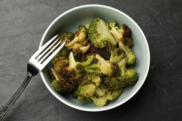 Tasty fried broccoli and fork on black table, top view