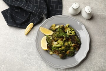 Tasty fried broccoli, shakers and lemon on light grey table, flat lay