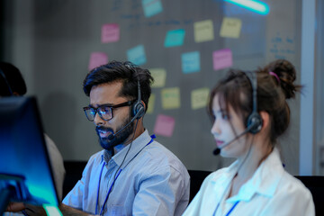 A diverse team of customer support agents works a late shift in a modern call center. Focused...