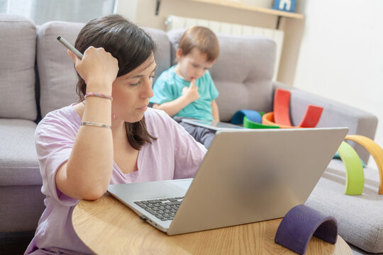 Stressed mother working from home as child uses tablet in background