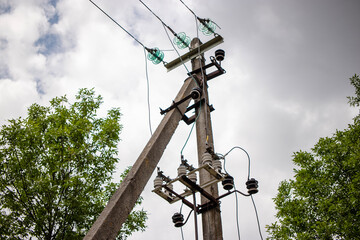 Utility pole with electrical lines and green trees against a cloudy sky in a rural setting