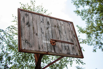 Old basketball hoop stands abandoned in a park surrounded by trees during a cloudy day
