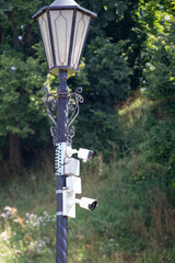 Security cameras mounted on a vintage street lamp in a public park providing surveillance and safety