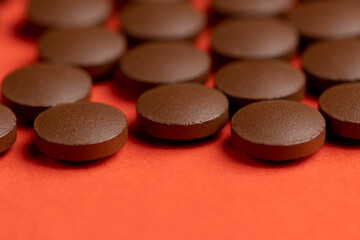 brown tablets lying on orange paper without packaging, a large number of brown tablets as medicine on an orange-colored paper surface