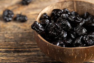black prunes made from ripe blue plums in a coconut shell plate, dried plums in a bowl made from natural materials