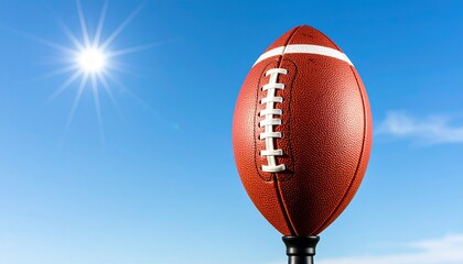 American football ball standing upright on a kicking tee against a clear blue sky with strong sunlight creating sharp shadows