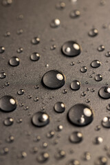 a black plastic surface covered with water drops, details of the wet part of an object made of...