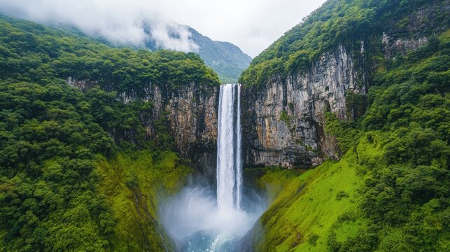 Gocta waterfall creates a misty spectacle as it plunges from a towering cliff into the valley below, surrounded by vibrant green vegetation and a cloudy sky