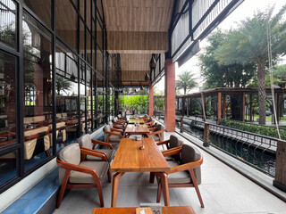 Cozy outdoor restaurant seating with wooden tables and chairs on a patio overlooking a tranquil canal and lush greenery